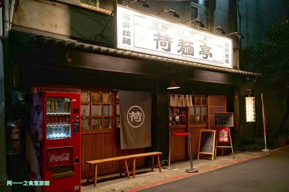 Hasumentei’s Shilin storefront at night, with the illuminated 荷麵亭 sign above wooden doors, a red vending machine, and an empty bench.