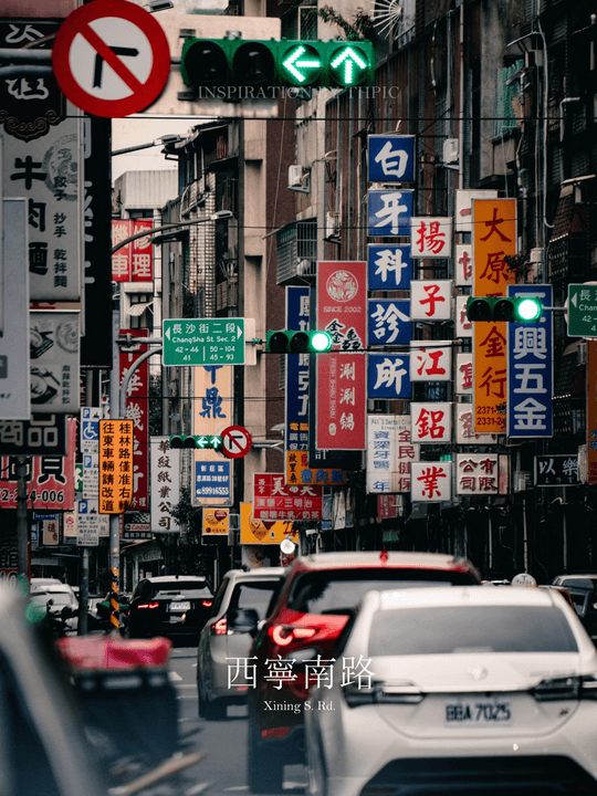 A telephoto view down Taipei’s Xining South Road, with cars and dense layers of Chinese storefront signs beneath green traffic signals.